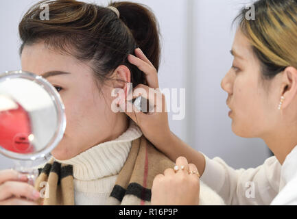Shanghai, China. 9 Nov, 2018. Ein Aussteller hilft einer Frau bei dem Versuch, Ohrringe auf der Bekleidung, Accessoires & Konsumgüter bereich der ersten China International Import Expo (CIIE) in Shanghai, China, November 9, 2018. Credit: Li Er/Xinhua/Alamy leben Nachrichten Stockfoto