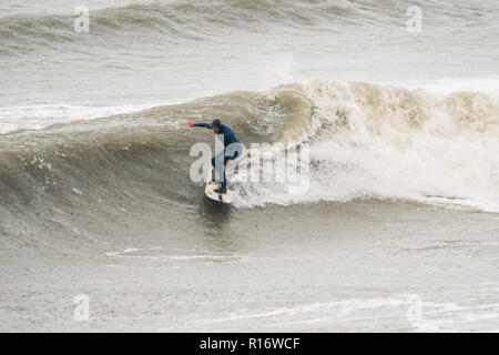 Aberystwyth Wales UK, 10/11/2018.de Wetter: Eine wilde, nassen und stürmischen Morgen in Aberystwyth, mit riesigen Wellen bei Flut entlang der Promenade und Meer Verteidigung der Küstenstadt auf die Cardigan Bay, West Wales. Lokale pro Surfer LEIGH DENYER macht den meisten starker Dünung und fängt den Wellen. Foto Keith Morris/Alamy leben Nachrichten Stockfoto