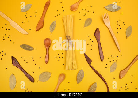 Handgefertigten Holz- Utensilien, Nudeln und Gewürzen. Flach Zusammensetzung auf gelben Hintergrund. Stockfoto