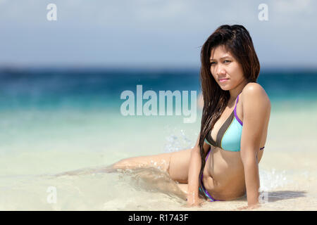 Schöne junge Filipina Frau am Meer in den flachen ruhigen blauen Ozean sitzen in einem Bikini genießen Sie die warme tropische Sonne, mit copysp Stockfoto