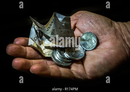 Indonesien, rupiah kleine Bill und Münzen in der Hand eines asiatischen Person isoliert. Konzept der Betteln für verlassen, schlechte Person. Stockfoto