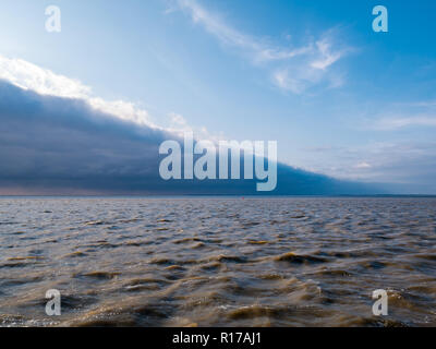 Vorderkante mit Linie der Sturmwolken des kalten Wetters vorne nähert sich blauer Himmel auf rauen Wasser des Wattenmeer, Niederlande Stockfoto