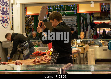 Junge Metzger hacken rohes Fleisch mit einem Fleischspalter auf einem Markt in Leeds, West Yorkshire, England, Großbritannien. Stockfoto