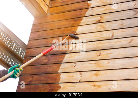 Man lackieren Holzbretter mit einem Bogen Walze und Schaumstoffrolle. Braun Farbe lackiert ist oder auf eine Holzwand gerollt Stockfoto