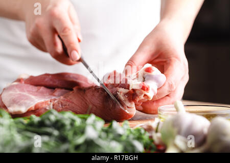 Das Konzept der Kochen Fleisch. Der Küchenchef, der Metzger, schneidet rohes Fleisch mit Rind, Lamm, Kalb und hielt ein Messer in der Hand, auf einem Holztisch, neben liegen r Stockfoto