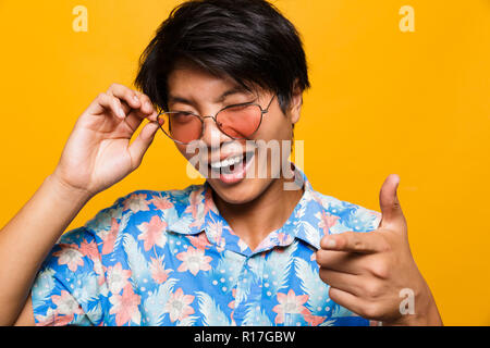 Nahaufnahme, Porträt einer fröhlichen asiatischer Mann in Sonnenbrille über Gelb Hintergrund isoliert, winking Stockfoto