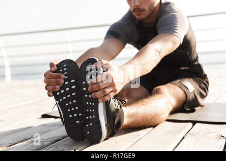 7/8 Foto der jungen gutaussehenden Mann im Freien Sport am Strand sport Dehnübungen. Stockfoto