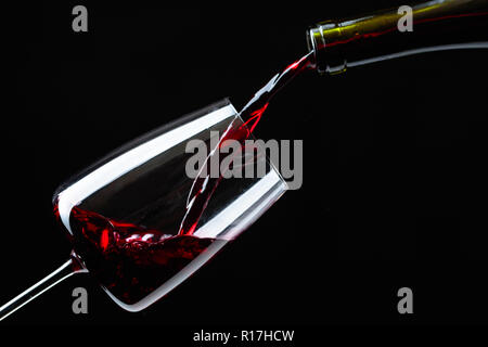 Rotwein in Glas Wein auf einem schwarzen Hintergrund gegossen. Stockfoto