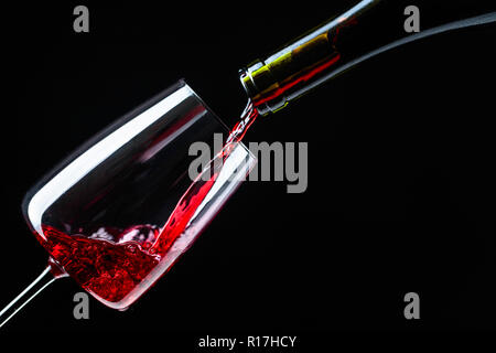 Rotwein in Glas Wein auf einem schwarzen Hintergrund gegossen. Stockfoto