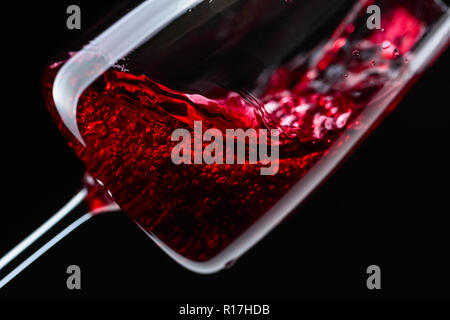 Rotwein in Glas Wein auf einem schwarzen Hintergrund gegossen. Stockfoto