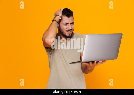 Porträt einer überrascht junge legerer Mann stehend über orange Hintergrund isoliert, Laptop Stockfoto