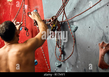 Mann Kletterer auf künstliche Kletterwand in Bouldern Fitnessraum Stockfoto