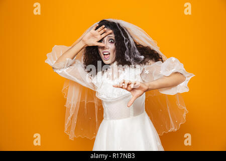 Verängstigte Frau Zombie in Wedding Dress und viel Suchen und Verstecken mit den Händen über orange isoliert Stockfoto