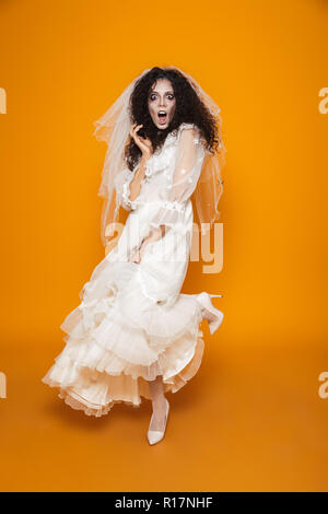 In voller Länge geschossen von verängstigten creepy Frau Zombie im weissen Brautkleid und viel suchen Kamera über orange isoliert Stockfoto