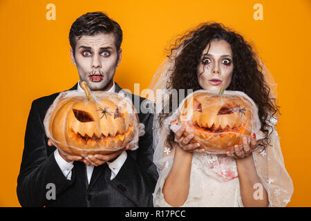 In voller Länge geschossen von creepy scary halloween Braut und Bräutigam in Hochzeit Kostüme, Kamera und Holding Kürbis in Web über orange isoliert Stockfoto