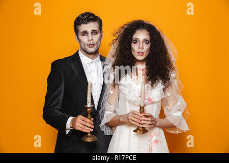 Foto von Spooky zombie Paar Bräutigam und Braut tragen Outfit und Halloween Make-up Holding Kerzen über Gelb Hintergrund isoliert Stockfoto