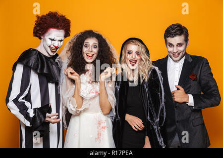 Gruppe von Fröhlichen Freunden in gruselige Kostüme feiern Halloween gekleidet isoliert auf gelbem Hintergrund Stockfoto