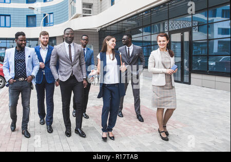 Erfolgreiche Unternehmen mit glückliche Arbeiter. Männer und Frauen in Anzügen stehen mit ihren Armen vor dem Hintergrund der Wolkenkratzer gekreuzt. Stockfoto