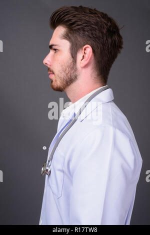 Die Jungen gut aussehenden bärtigen Mann Arzt gegen grauer Hintergrund Stockfoto