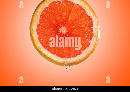 Nahaufnahme von rosa Grapefruit Slice mit Tropfen Saft, orange Farbe Hintergrund Stockfoto