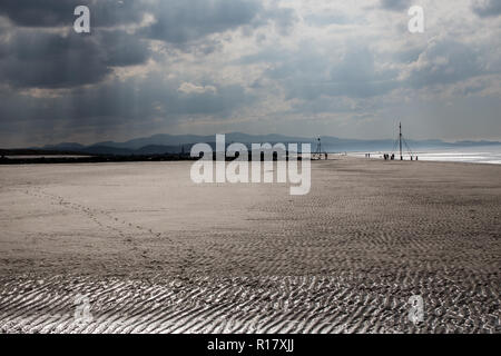 Leeren Strand an einem düsteren Moody Tag mit Sonnenstrahlen, die durch die stürmischen Wolken. Towyn Stadt und die Berge von Snowdonia sind sichtbar im Hinterg Stockfoto