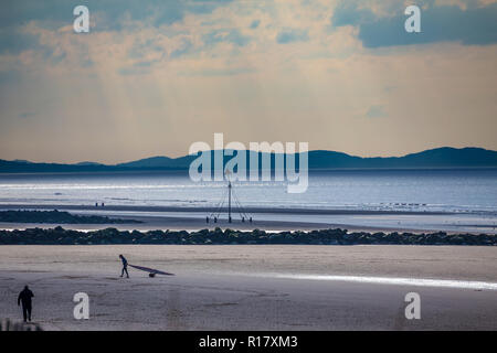 Leeren Strand an einem düsteren Moody Tag. Ein Mann zieht ein Kajak zurück zum Strand. In Prestatyn, North Wales, UK, 2018 getroffen Stockfoto