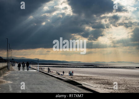 Leeren Strand an einem düsteren Moody Tag mit Sonnenstrahlen, die durch die stürmischen Wolken. Towyn Stadt und die Berge von Snowdonia sichtbar sind. Stockfoto