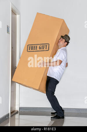 Der Postbote trägt eine große Paket - Freies Geschenk. Der E-Mail-Dienst trägt eine große Lieferung in die Wohnung. Stockfoto