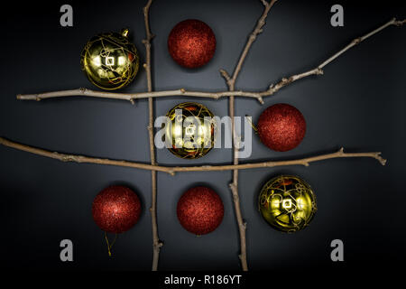 Tic-Tac-Toe Spiel mit trockenen Zweigen und Weihnachten rot und goldenen Kugeln auf schwarzem Hintergrund. Stockfoto