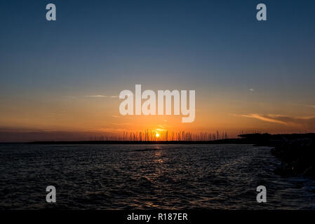 Horizontale Foto mit Sonnenuntergang Dämmerung über das Mittelmeer. Sonne ist im Hintergrund hinter Stein Pier, wo mehrere Boote und Schiffe ankern. Himmel klar ist w Stockfoto