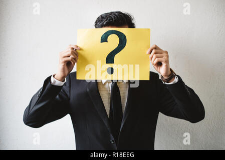 Junge Erwachsene asiatische Geschäftsmann Holding gelbe Schild Papier mit Fragezeichen. Konzept der Business FAQ und Fragen Stockfoto