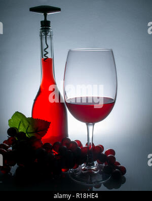 Wein in einem Glas neben einer Flasche Wein und Trauben auf einem Tisch mit Überlegungen über einen vintage Wand Hintergrund Stockfoto