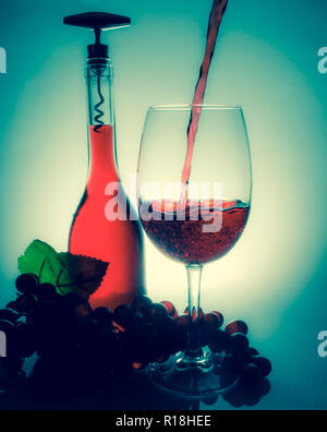 Gießen Wein in einem Glas neben einer Flasche Wein und Trauben auf einem Tisch mit Überlegungen über einen vintage Hintergrund Stockfoto
