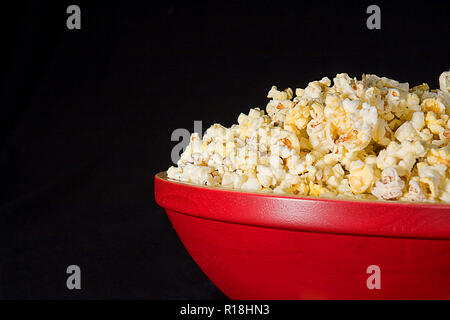 Große rote hölzerne Schüssel Popcorn auf schwarzem Hintergrund isoliert.