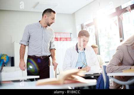 Ernsthafte Lehrer suchen an einer der Schüler von Notizen während der individuellen Arbeit in der Klasse Stockfoto