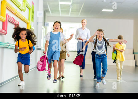 Adorable glückliche Schülerinnen und Schüler von der Schule Korridor zusammen mit Lehrer hinter Stockfoto