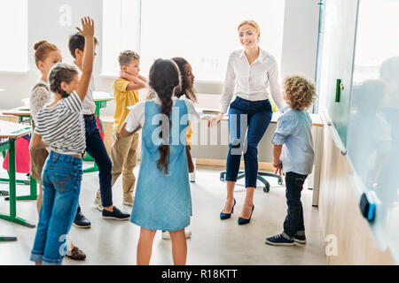 Gruppe von Mitschülern um Lehrer im Klassenzimmer und Spaß haben Stockfoto