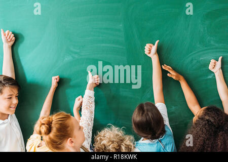 7/8 shot der Schulkinder mit Daumen hoch Vor leere Schiefertafel Stockfoto
