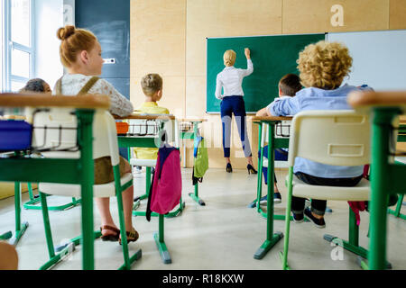 Ansicht der Rückseite des Schüler Lehrer suchen, während Sie schreiben auf der Schiefertafel Stockfoto