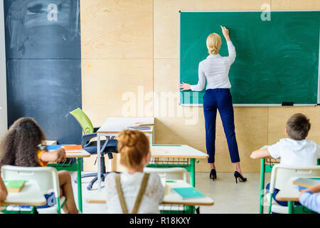 Ansicht der Rückseite des Schüler Lehrer suchen, während Sie schreiben auf der Schiefertafel Stockfoto