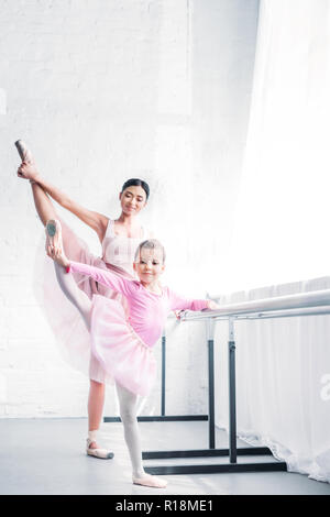 Lächelnden jungen Ballett Lehrer an der Kleine student Stretching und Kamera im Ballett Studio suchen Stockfoto