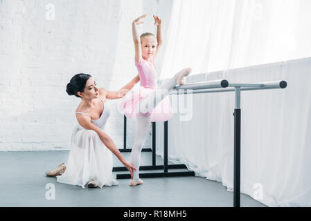 Adorable Kind in rosa Tutu Stretching und Kamera beim Üben Ballett mit Lehrer Stockfoto