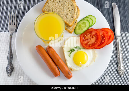 Das Frühstück auf dem Tisch Spiegelei in einer Herzförmigen gebratene Würstchen, frisch geschnittenes Gemüse Gurken und Tomaten, Saft, geschnittenem Brot, Messer und Gabel, Stockfoto