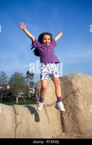 Junge Mädchen Sprung vom Felsen auf dem Spielplatz. Herr © Myrleen Pearson... Ferguson Cate Stockfoto