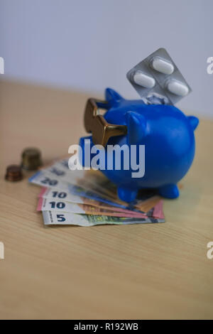 Cool Blue Sparschwein mit goldenen Brille mit Pillen und Euro-münzen und Hinweis auf hölzernen Tisch isoliert, Schatz Stockfoto