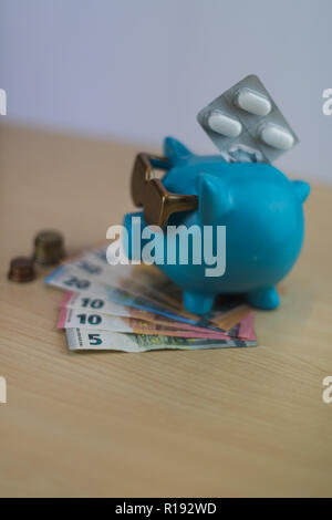 Kühlen türkis Sparschwein mit goldenen Brille mit Pillen und Euro-münzen und Hinweis auf hölzernen Tisch isoliert, Schatz Stockfoto