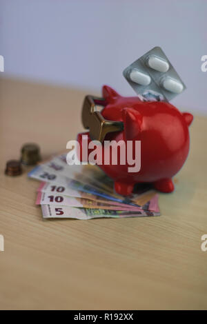 Coole rote Sparschwein mit goldenen Brille mit Pillen und Euro-münzen und Hinweis auf hölzernen Tisch isoliert, Schatz Stockfoto