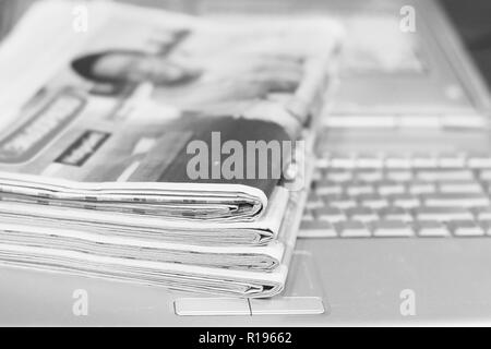 Zeitungen und Laptop. Stapel von Zeitungen mit Nachrichten auf dem Computer. Seiten mit Schlagzeilen, Artikel gefaltet und auf der Tastatur der elektronischen Gerät gestapelt Stockfoto