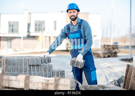 Builder in Uniform, die Pflastersteine von der Palette auf der Baustelle im Freien Stockfoto