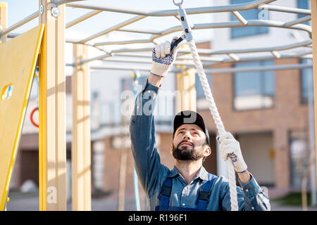 Stattliche Arbeiter in Uniform die Seil zum Klettern auf dem Spielplatz im Freien Stockfoto